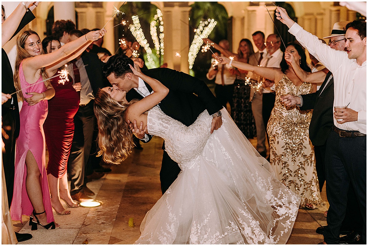 Newlyweds kissing during a sparkler exit surrounded by wedding guests