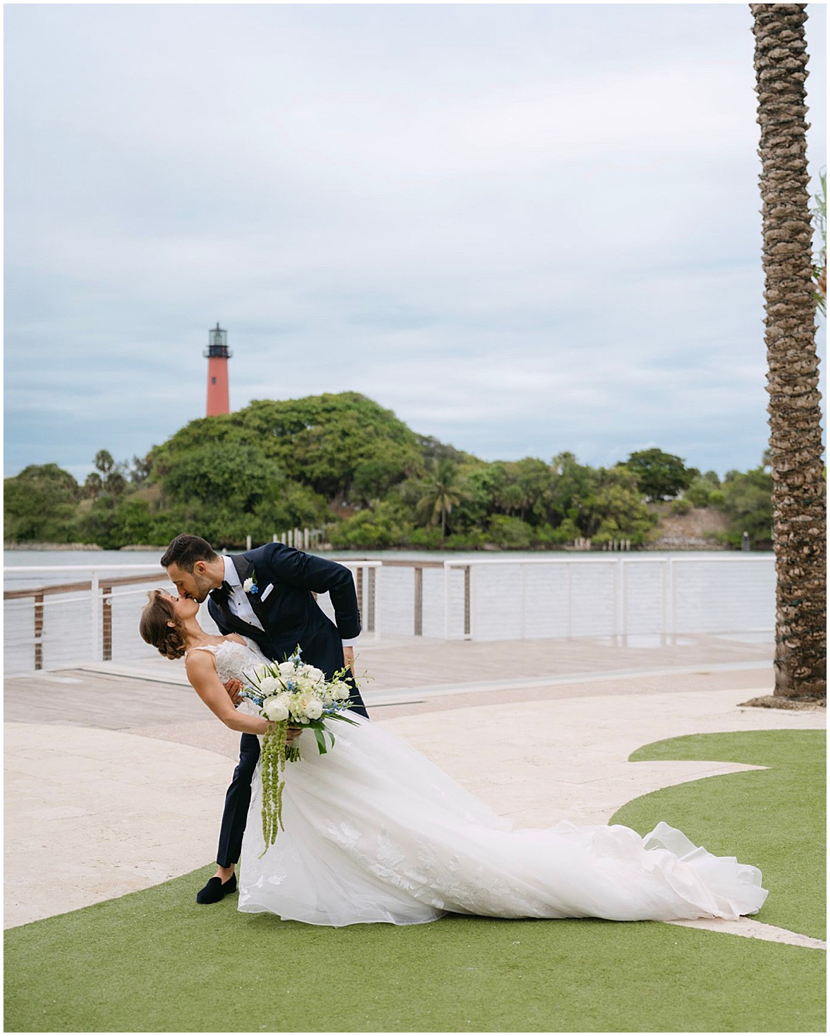 Bride and groom posing by the water with the Jupiter Inlet Lighthouse in the background.
