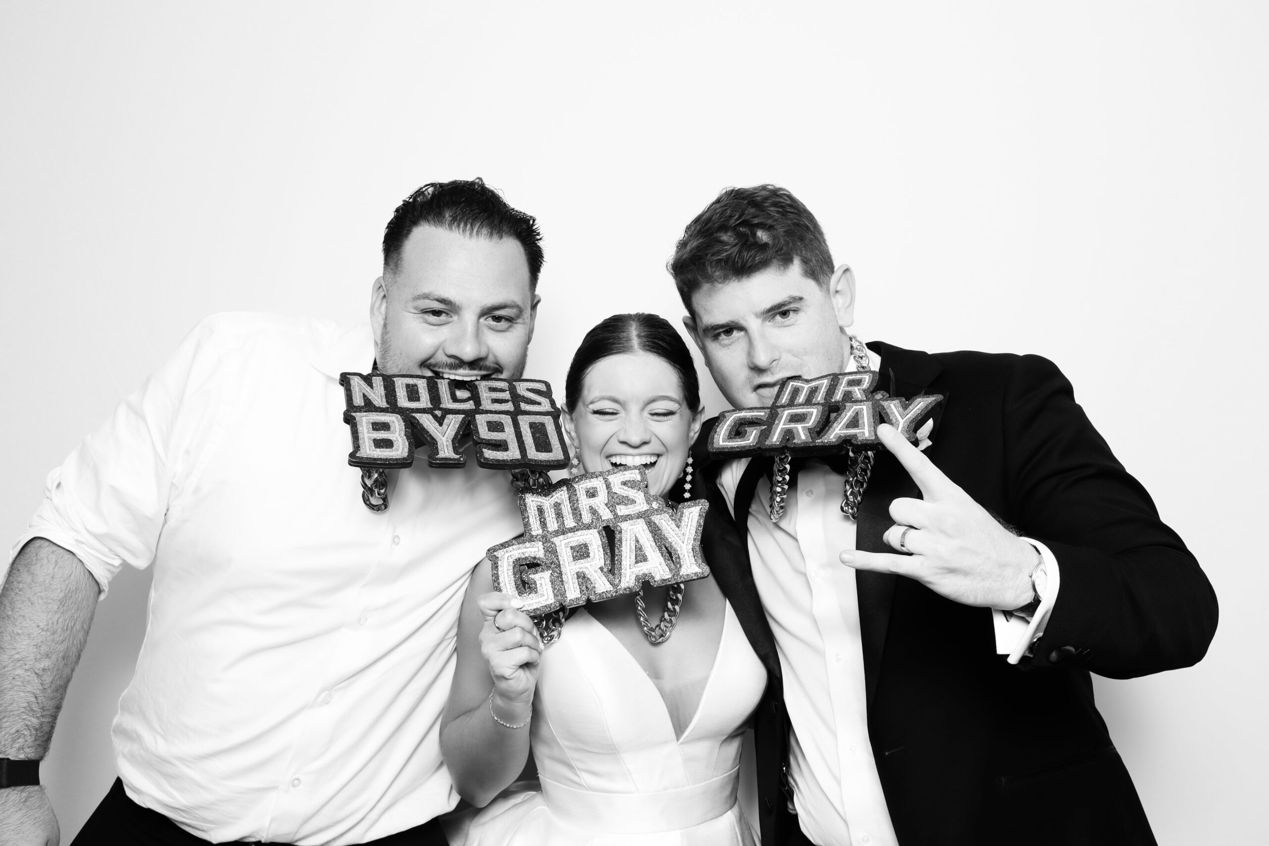Bride and groom holding a Noles by 90 prop in a black and white wedding photo booth